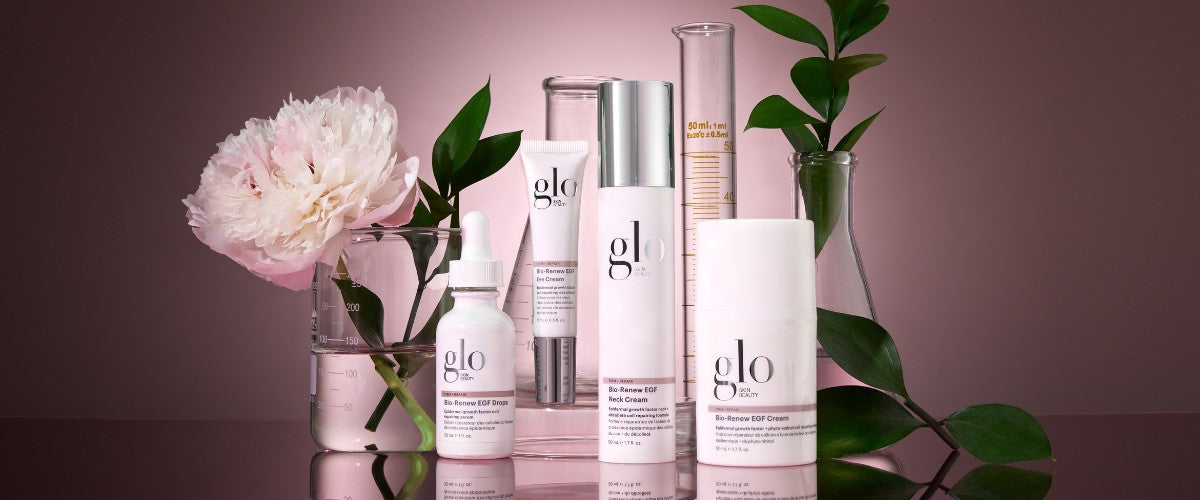 Glo skin beauty Bio-Renew EGF Drops, Neck Cream and EGF Cream arranged with beakers, peony and leaves on pink background