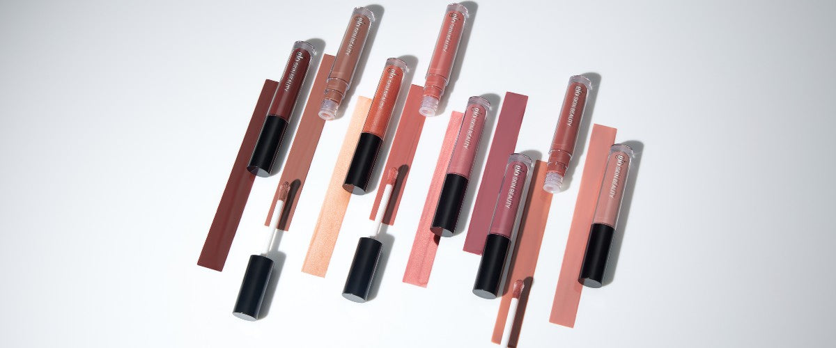 Lip-gloss tubes and applicators arranged with matching mauve, peach, and nude swatches on white background.