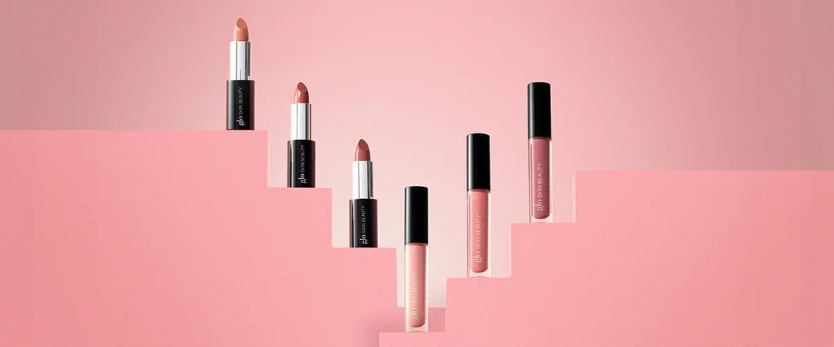 Five neutral-pink lipsticks and glosses arranged on pink stepped platforms