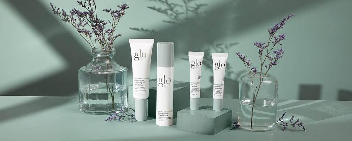 Front view of Glo skincare tubes and pump showing white packaging on mint green background with glass vases