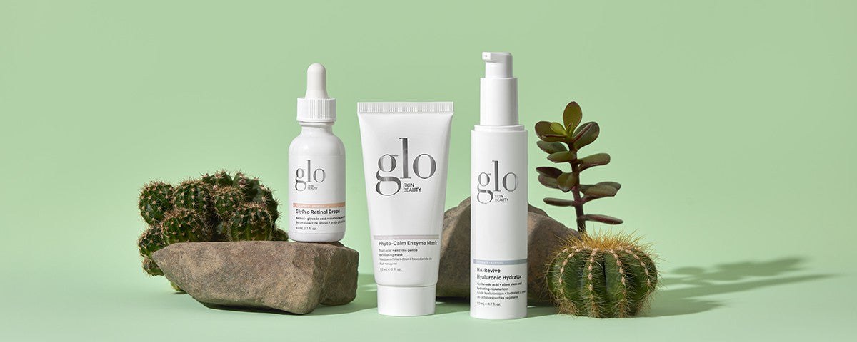 Three Glo Skin Beauty products on rocks with cacti: Phyto-Retinol Drops, Phyto-Calm Enzyme Mask, and HA-Revive Hydrator