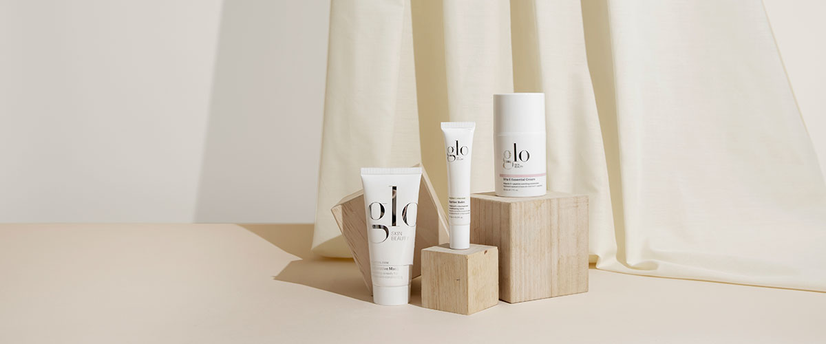 Three glo SKIN BEAUTY skincare products on wooden blocks with cream draped fabric background