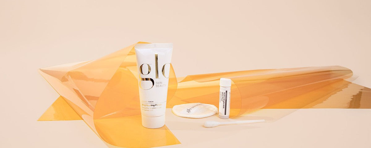 glo SKIN BEAUTY tube, small vial, cotton pad and spatula arranged on orange translucent film backdrop