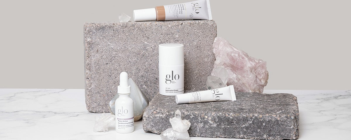 Assorted glo skincare bottles and tubes on stacked stone slabs with rose quartz crystals