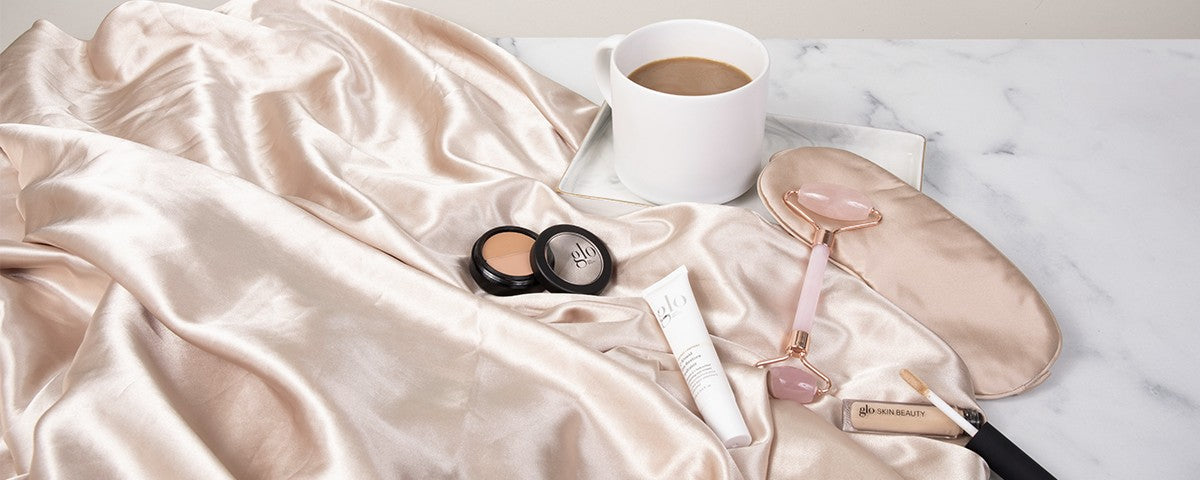 Silk pillowcase, satin eye mask, rose quartz jade roller, under-eye concealer and a cup of coffee with glo SKIN BEAUTY products