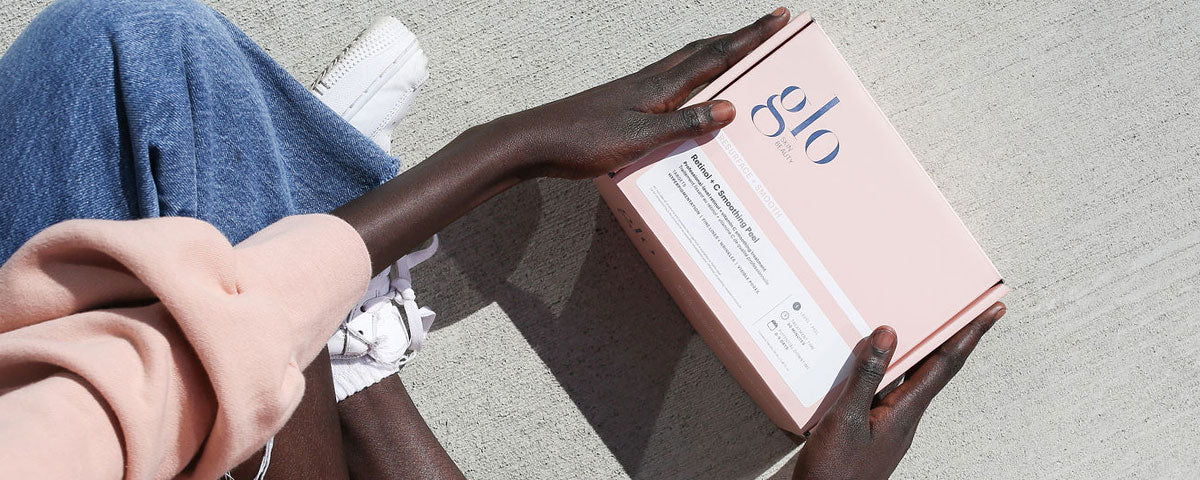 Hands holding a pink 'glo' skincare box labeled 'Retinol + Smoothing Peel' on concrete surface.
