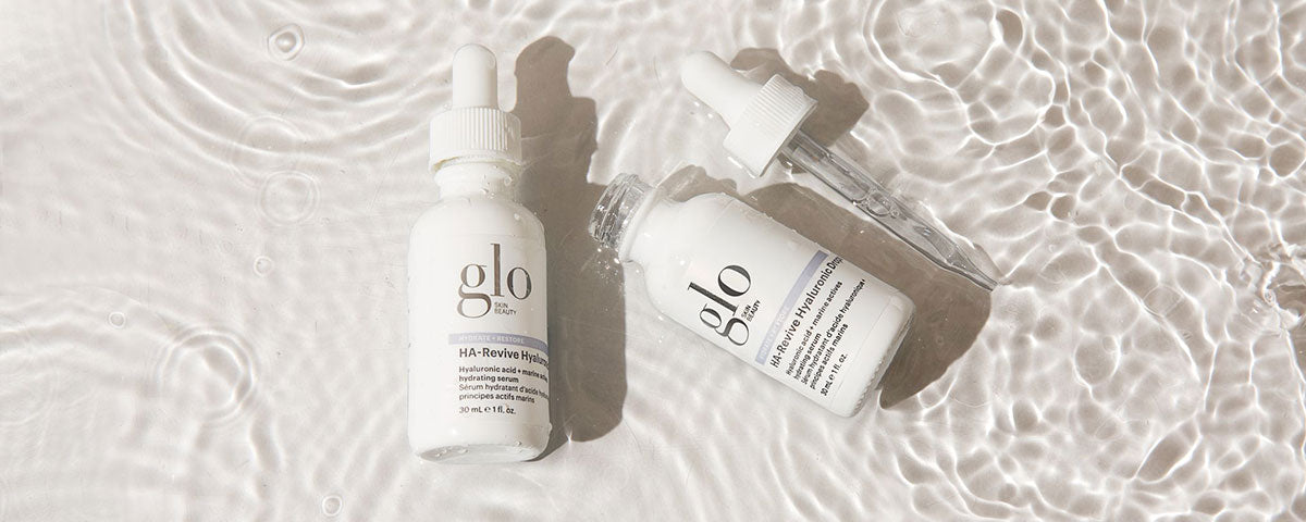 Two glo SKIN BEAUTY HA-Revive Hyaluronic serum bottles and dropper on rippling water surface