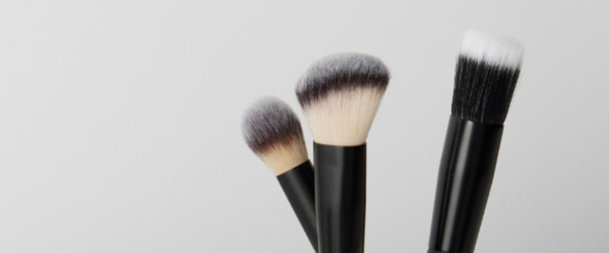 Three synthetic makeup brushes with black handles and two-toned bristles on a plain gray background