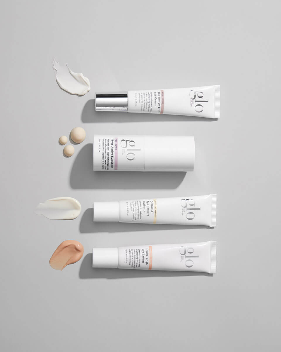 Four white glo skincare tubes with cream smears arranged vertically on a light gray background