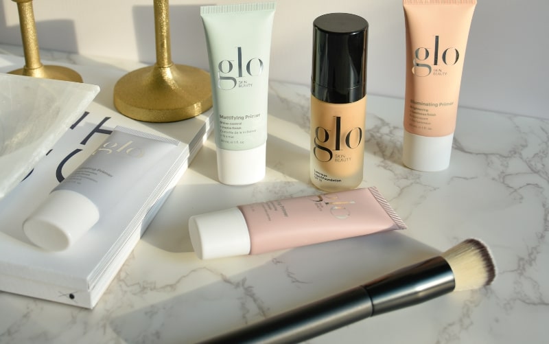 glo SKIN BEAUTY products on marble with brush; Mattifying Primer, Illuminating Primer and Sheer Foundation visible.