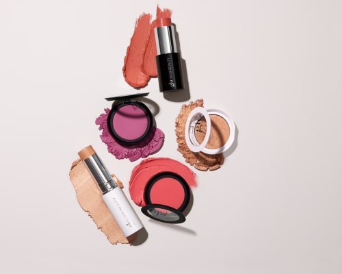 Assortment of cream and pressed blushes with swatches and compact pans arranged on a pale background.