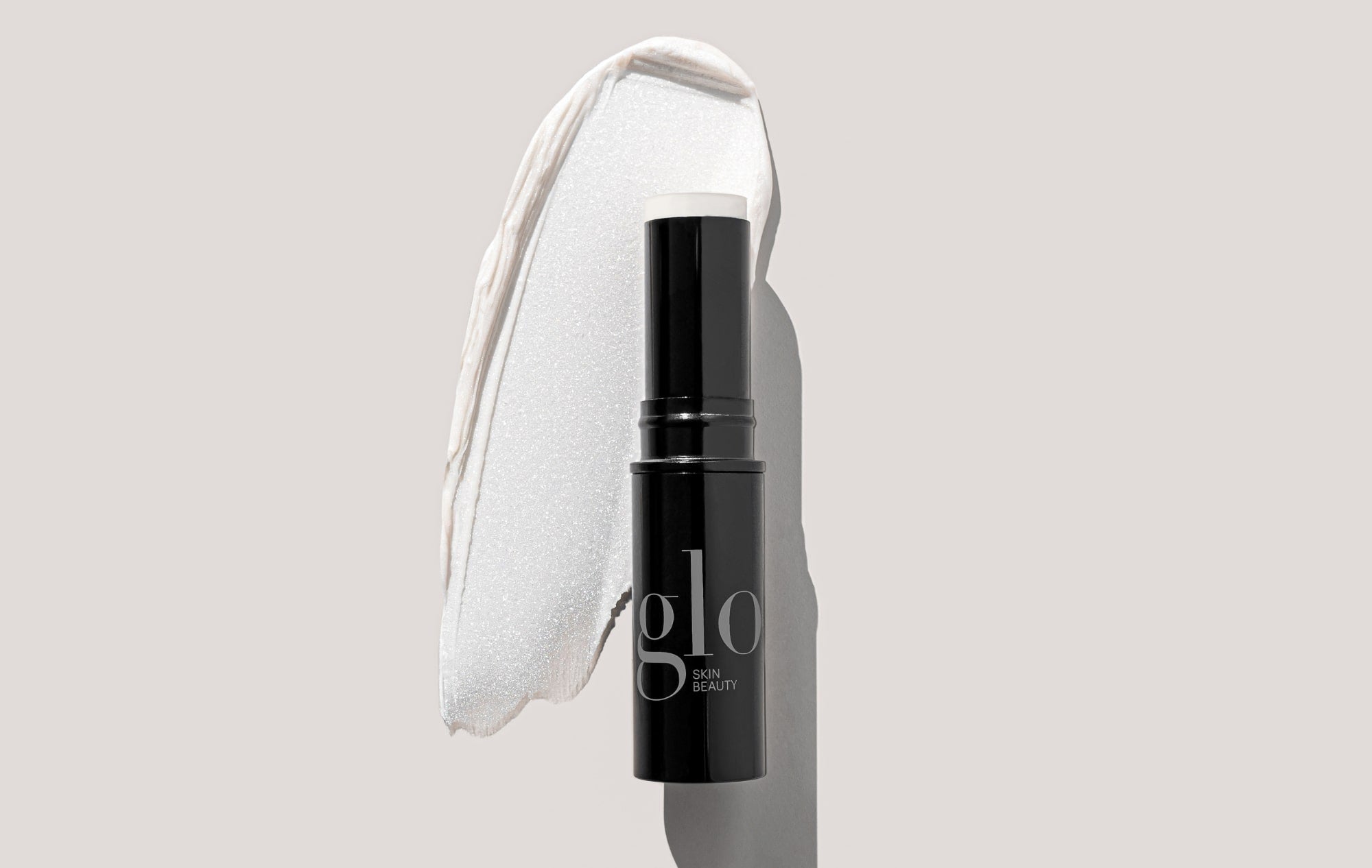 Black twist-up stick labeled glo SKIN BEAUTY with white balm exposed and a cream swatch behind it