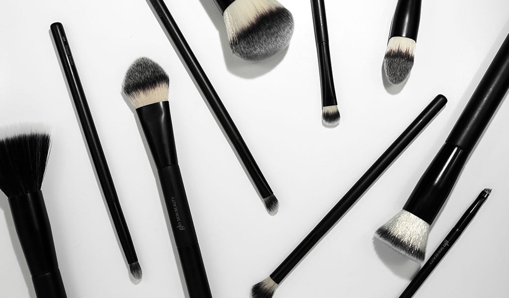 Assorted black-handled makeup brushes with white-and-gray bristles arranged on a white background.