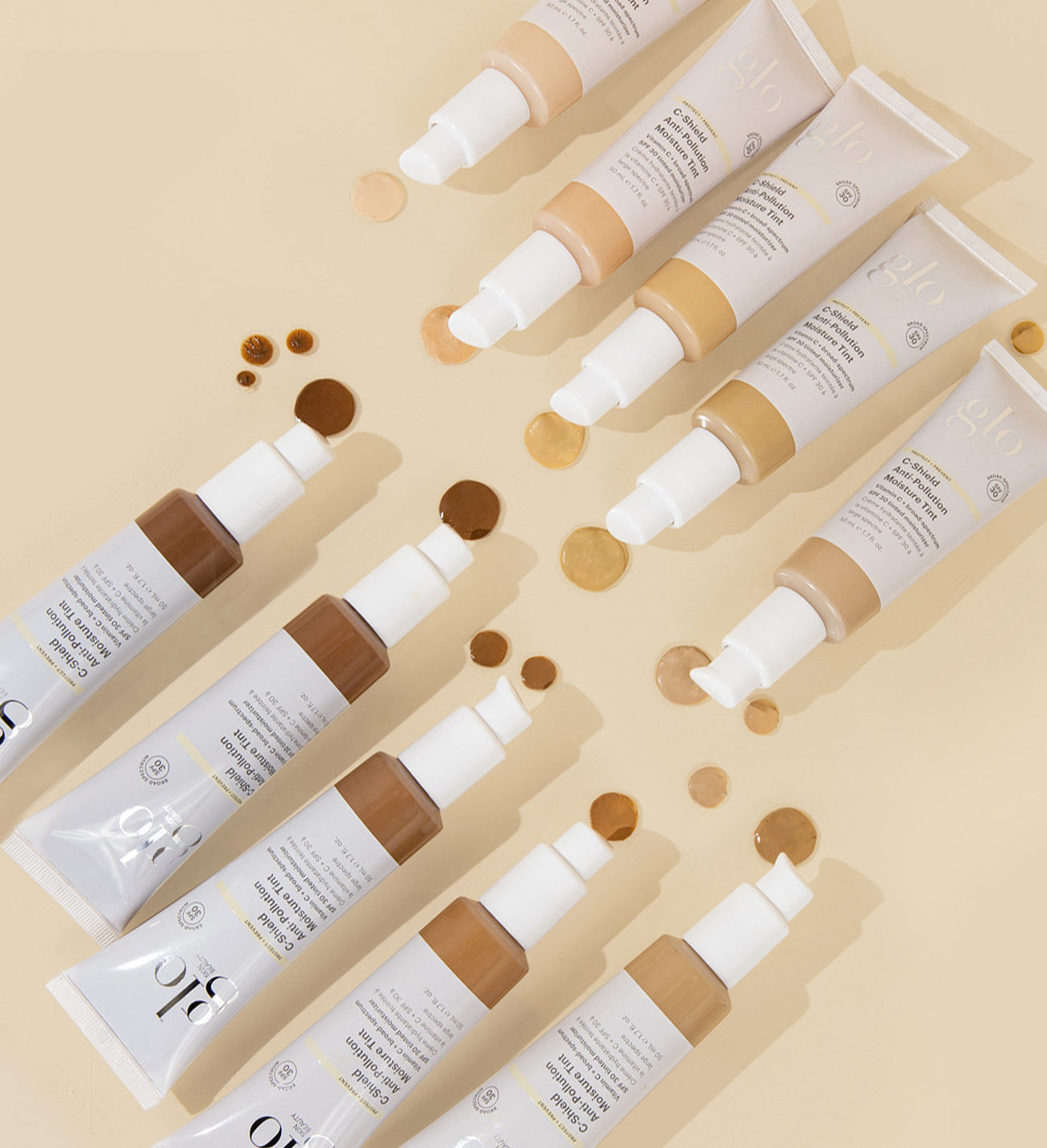 Rows of glo G-shield Anti-Pollution Moisture Tint tubes with foundation swatches in varying shades on beige background
