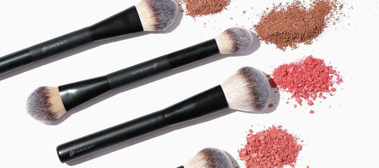 three black-handled makeup brushes with scattered brown and pink crushed powder