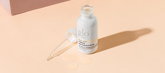 Dropper bottle labeled glo with clear serum pooled and dropper on peach background