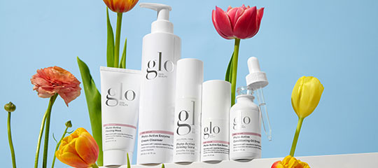 glo skincare bottles and tubes arranged on a white platform with colorful tulips against a blue background
