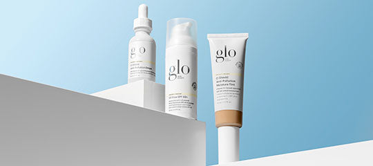 Three glo skincare products on white geometric pedestals against a pale blue background.