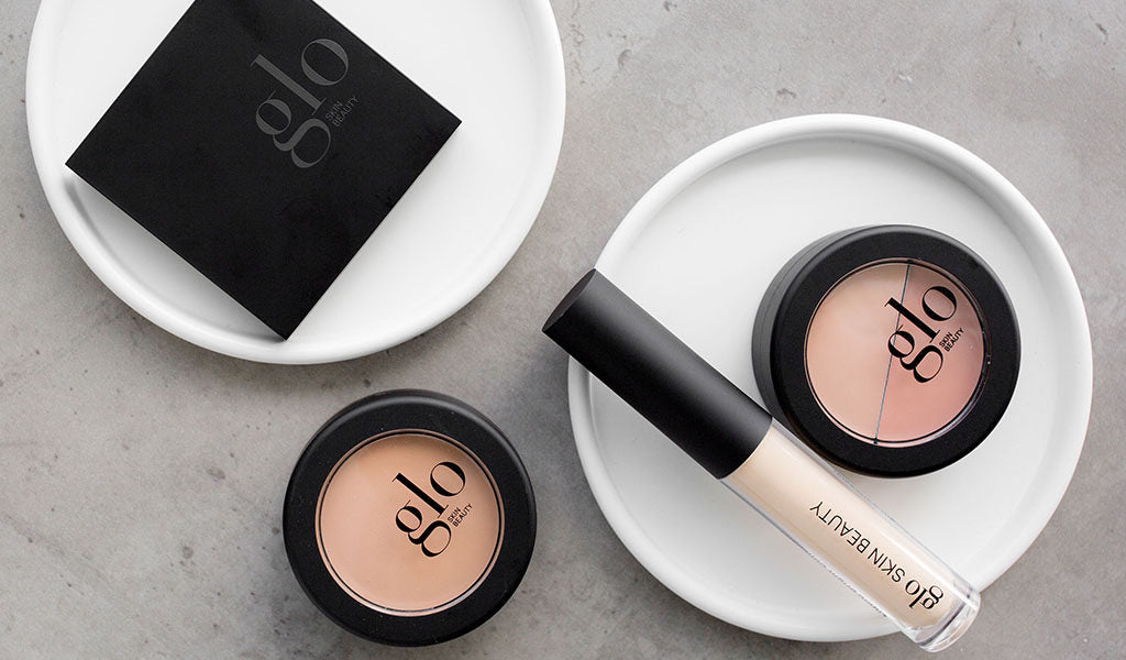 Three glo SKIN BEAUTY compacts and a glo SKIN BEAUTY concealer tube arranged on white dishes