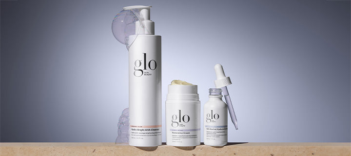 Three glo skin beauty skincare products: pump cleanser, jar cream, and dropper serum on pale gray background