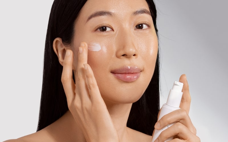Woman applying moisturizer to her cheek using a white pump bottle