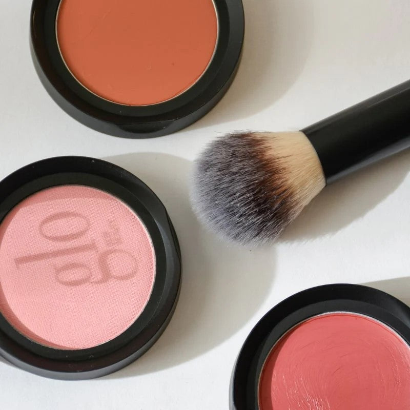 Three round blush pans (one pink pan shows 'glo' logo) and a fluffy makeup brush on white background
