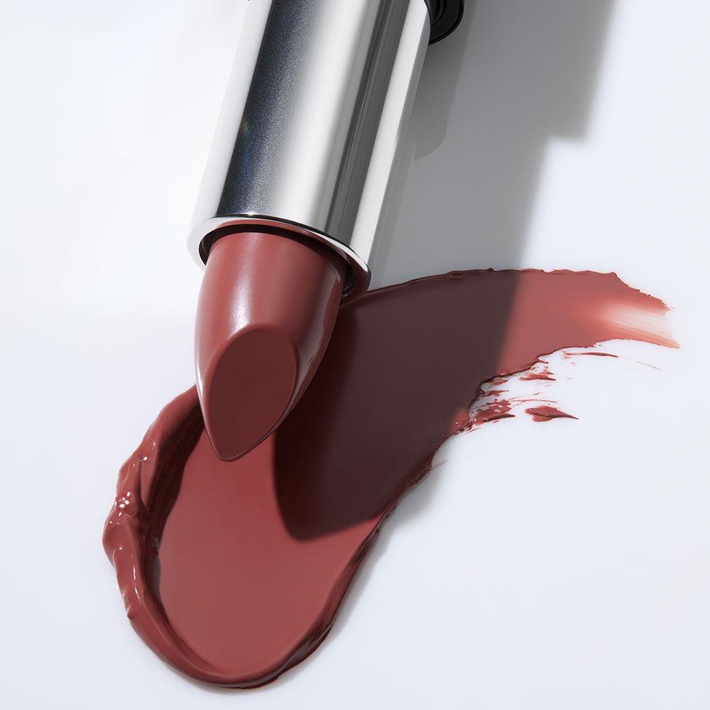 Close-up of mauve-red lipstick bullet with a smudged swipe on a white surface.