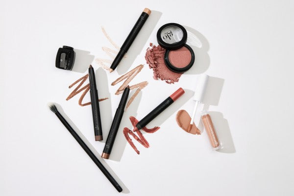 Makeup tools and products, including pencil eyeliners, blending brush, blush compact, lip crayon and a liquid swatch on white background