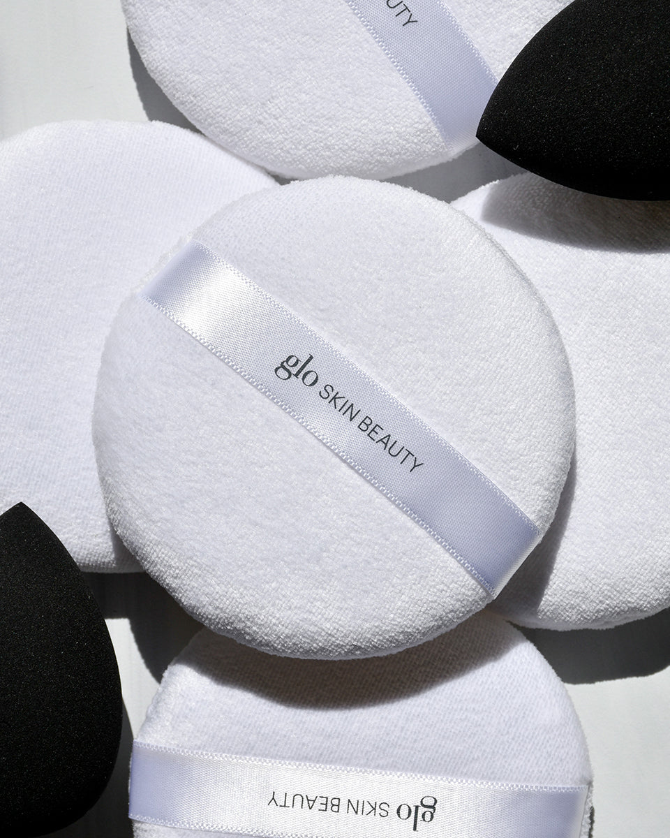 White powder puffs with 'glo SKIN BEAUTY' ribbons and black makeup sponges