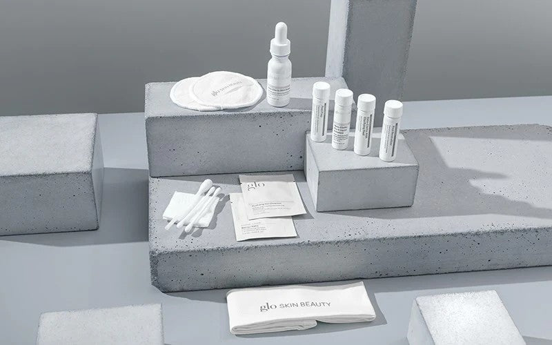 Skincare sample set and cotton swabs arranged on concrete display blocks, branded "glo SKIN BEAUTY" on a folded cloth.
