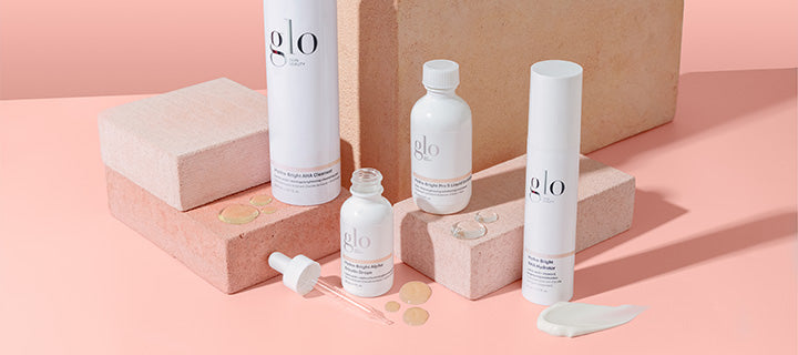 glo skincare bottles and dropper displayed on pink blocks with cream swatch and serum droplets