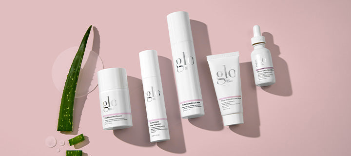 Glo Skin branded skincare bottles and tubes with aloe leaf and water droplets on pink background