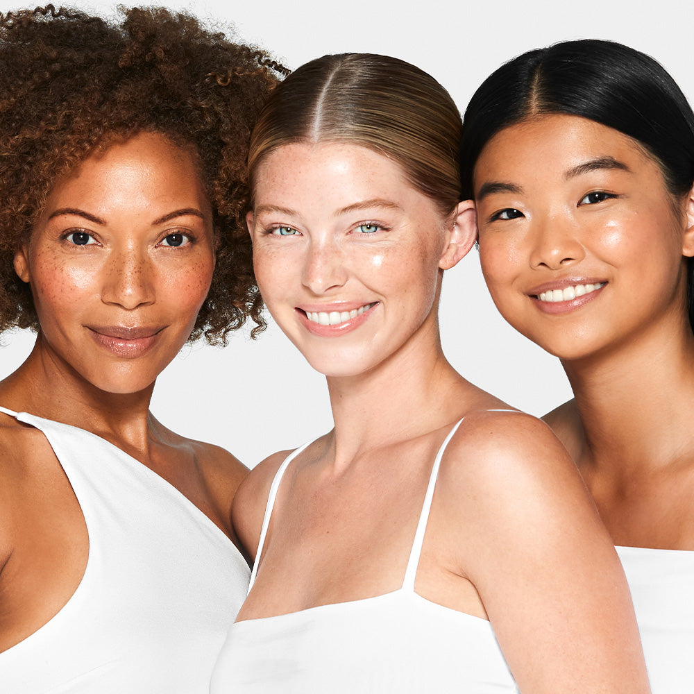 Three diverse women smiling in a close-up studio portrait wearing white tops