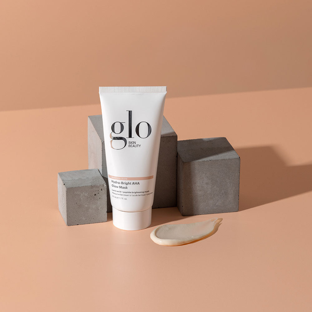 Tube of Glo Skin Beauty Hydra-Bright AHA Glow Mask with cream smear on peach background