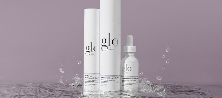 Three glo skin beauty HA-Revive Hyaluronic skincare bottles with water splashing on mauve background
