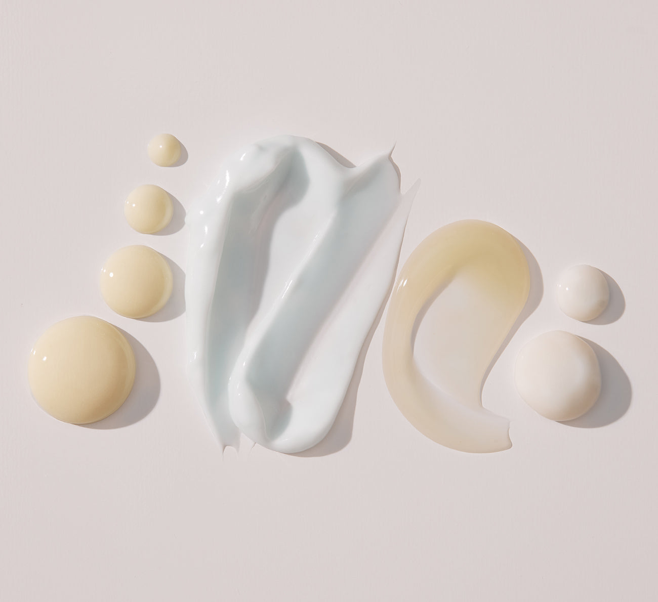Skincare product textures in white and beige swirls on a pale background
