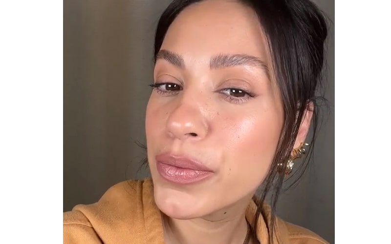Close-up of woman wearing warm nude lipstick, dewy skin, subtle eyeliner, hair pulled back and gold ear cuffs.