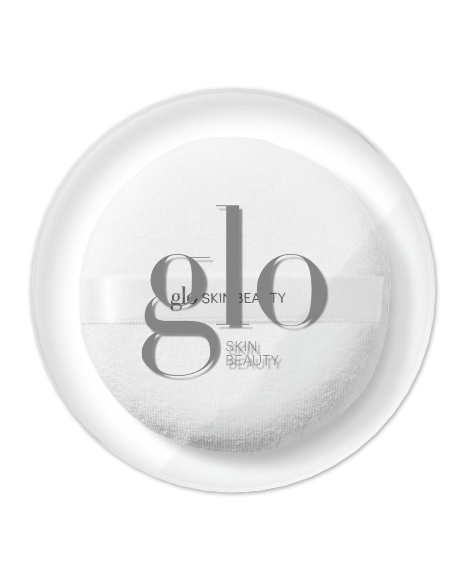 White powder puff with ribbon labeled 'glo SKIN BEAUTY' inside a clear round case