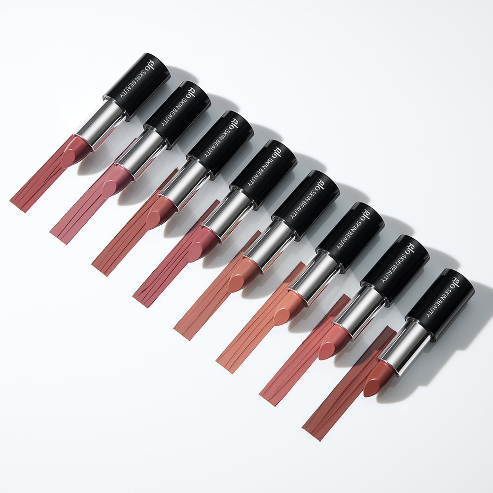 Eight GLO SKIN BEAUTY satin lipsticks arranged diagonally with matching swatches in neutral mauve and nude shades