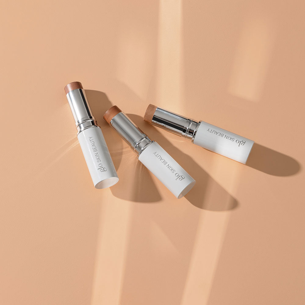 Three GLO SKIN BEAUTY cream bronzer sticks on a peach background with soft directional shadows