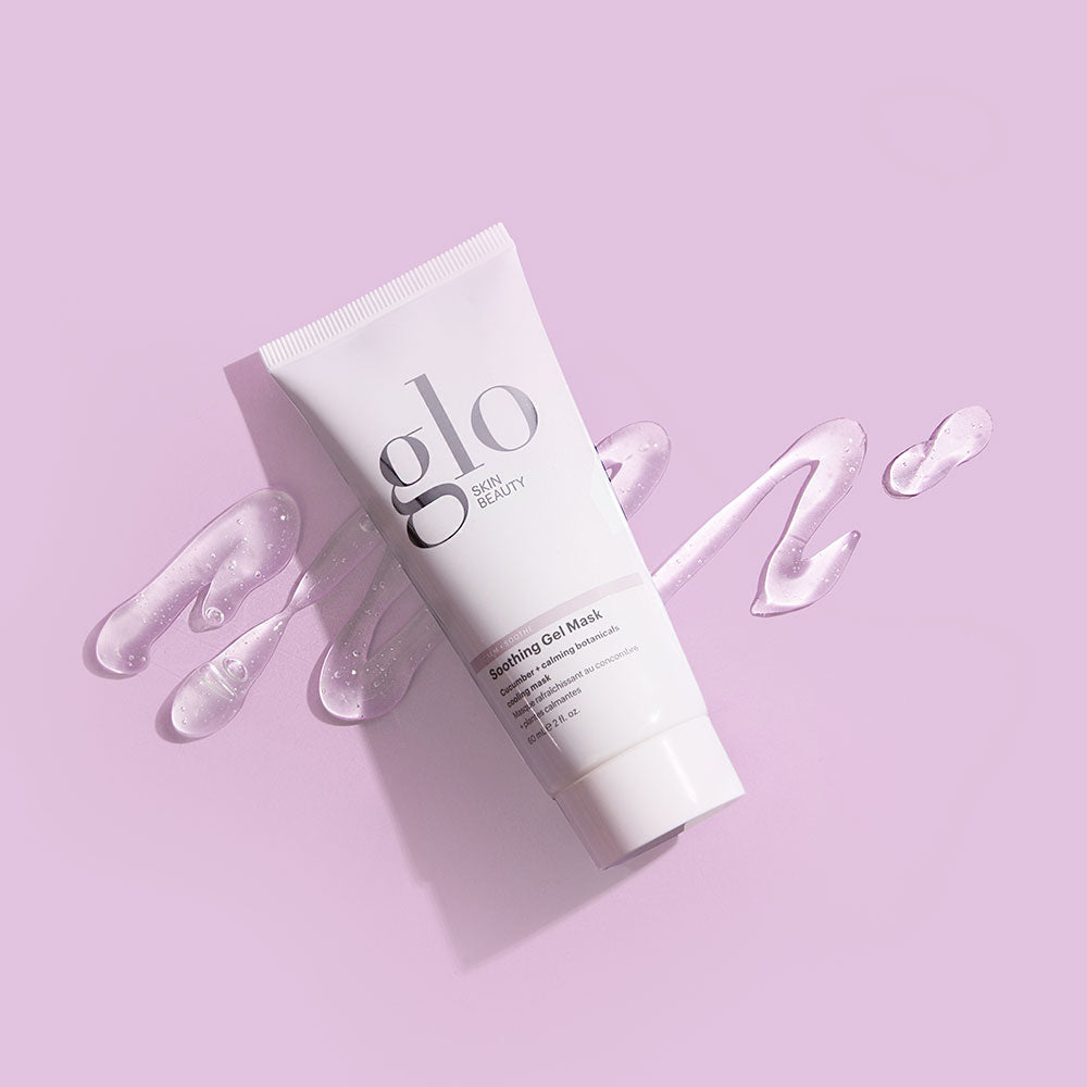 White tube labeled glo SKIN BEAUTY Soothing Gel Mask lying on pink background with clear gel swirls.