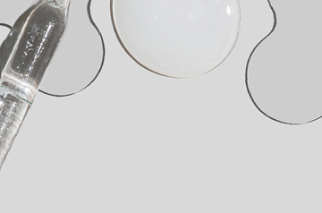 Clear glass dropper beside a shallow white dish and scalloped paint-palette wells on a light gray background