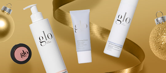 Assorted glo skincare products — pump bottle, tube, spray can and blush compact on gold background with ribbon and ornaments.