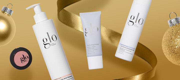 Three white Glo Skin Beauty products — pump labeled 'glo SKIN BEAUTY', tube 'Hydrating Primer', and spray on gold background