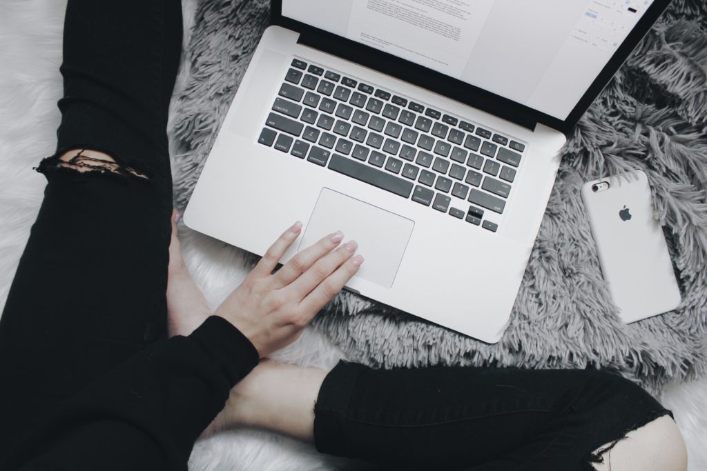 womans hand on laptop next to mobile phone