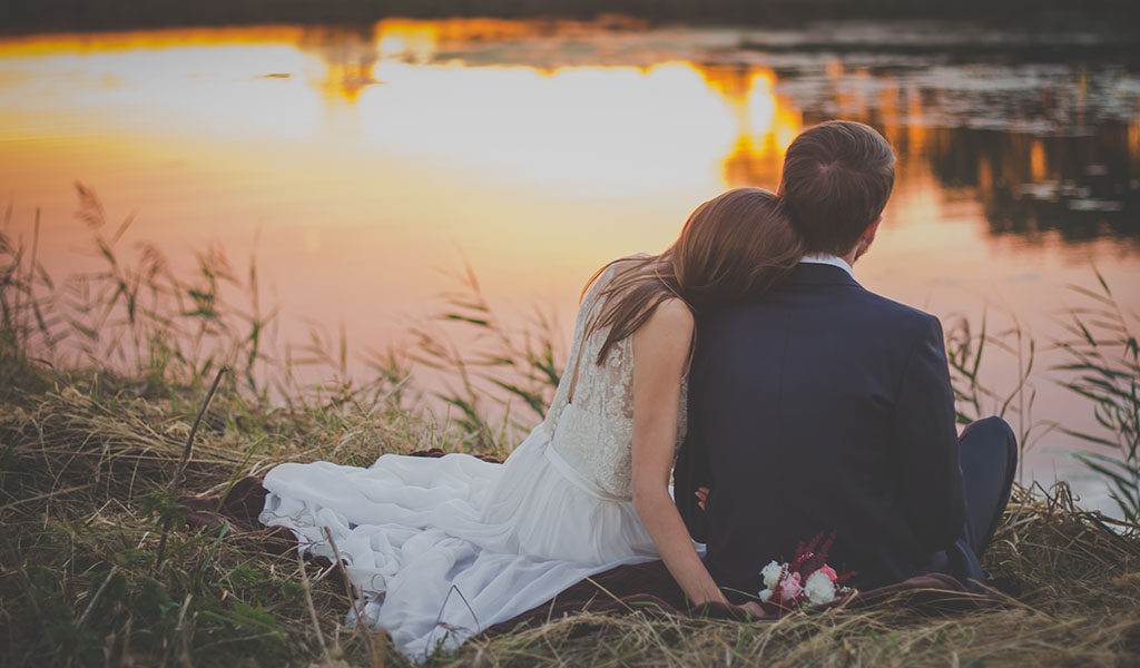 Bride and groom sitting by lake