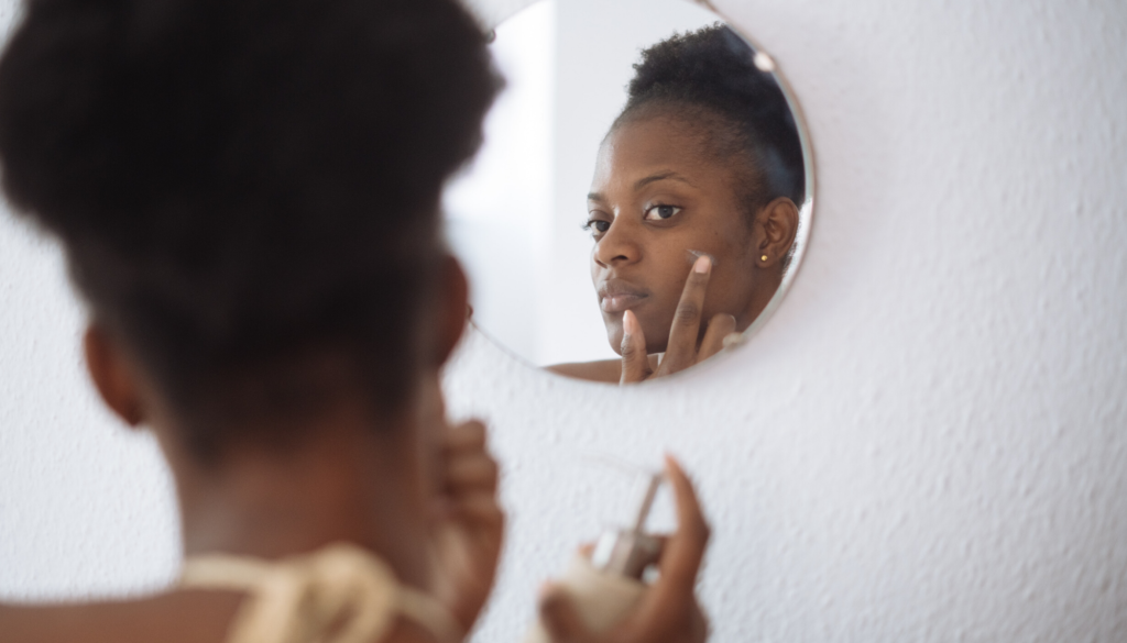 woman looking into mirror applying product