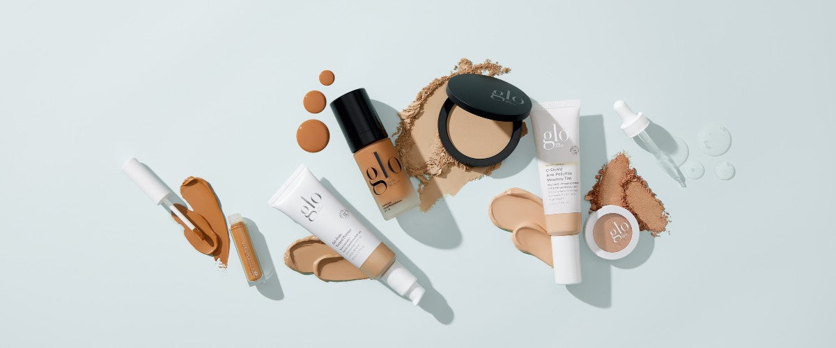 Assortment of glo-branded foundations, powders, droppers and swatches on a pale blue background.