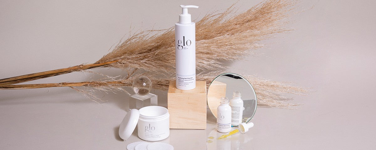 glo skincare bottles, jar, and dropper displayed with pampas grass and a small round mirror on a neutral surface