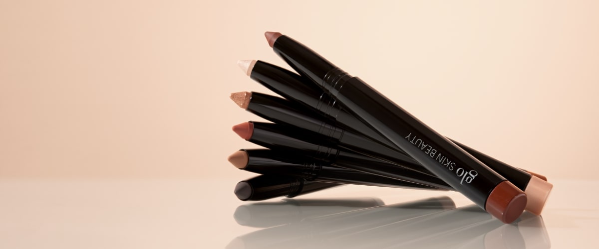 Set of black retractable eye-crayon pencils in neutral shades fanned on a reflective surface; Glo SKIN BEAUTY visible on one pen